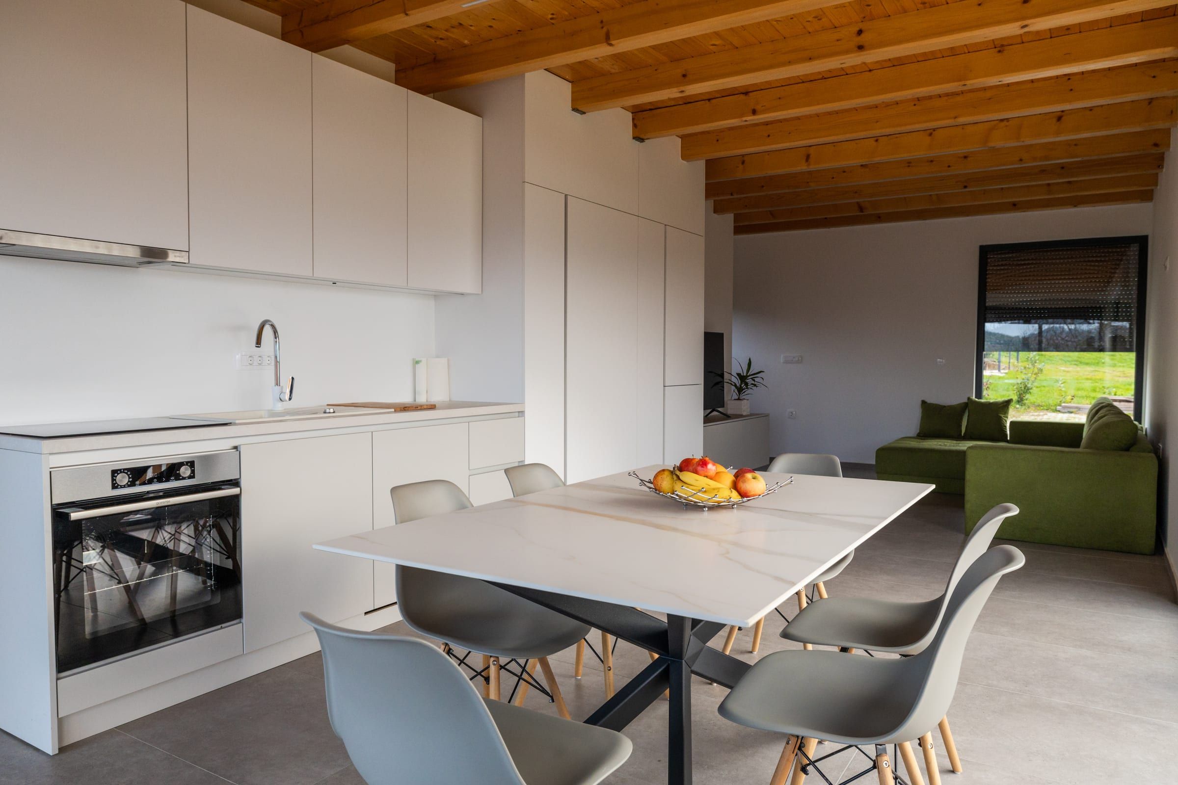 A wide view across the kitchen, dining table, and living room, with vineyard hills through the windows.