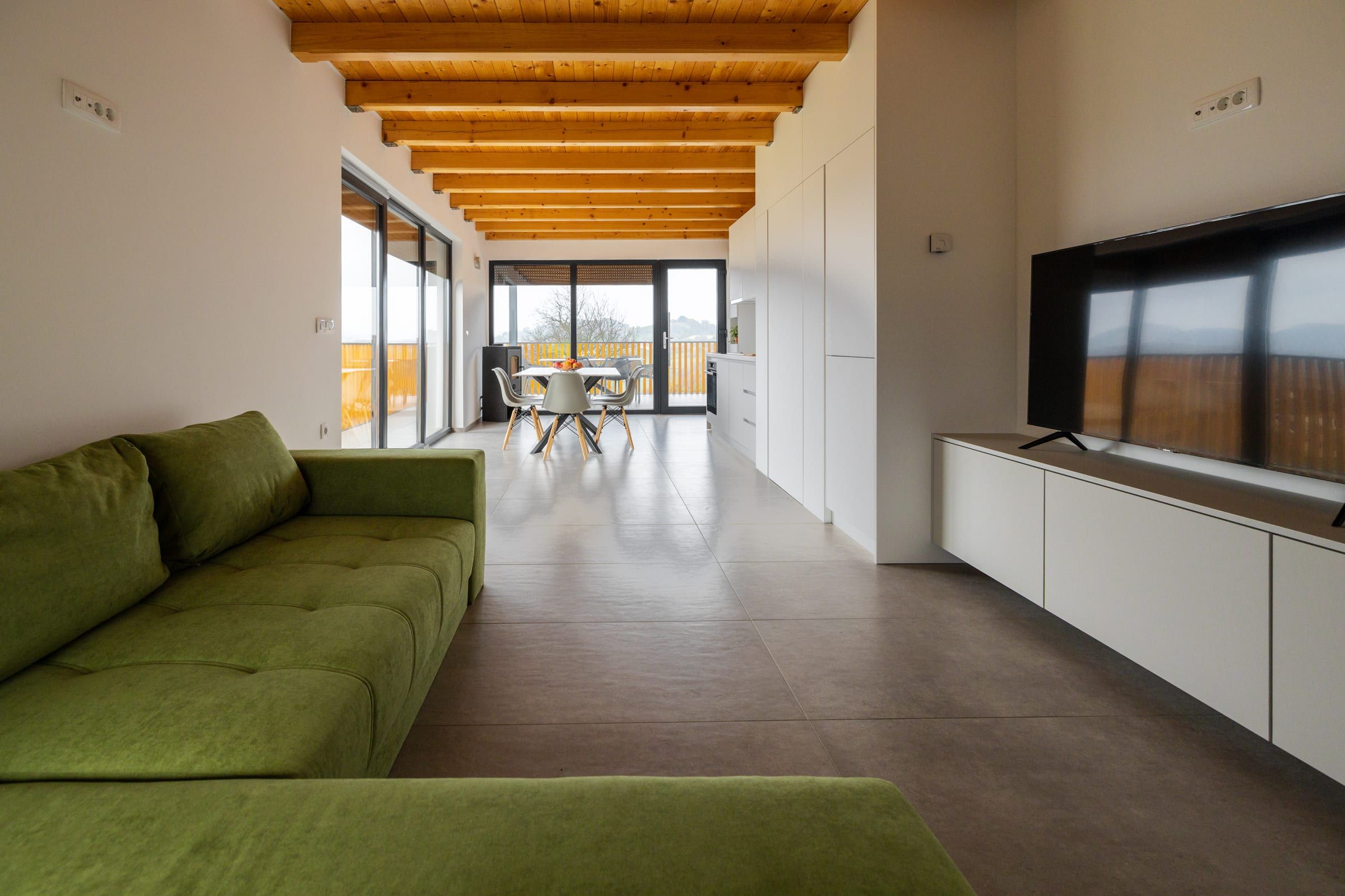 The living area with a green sofa, flat-screen TV, and timber-beamed ceiling.