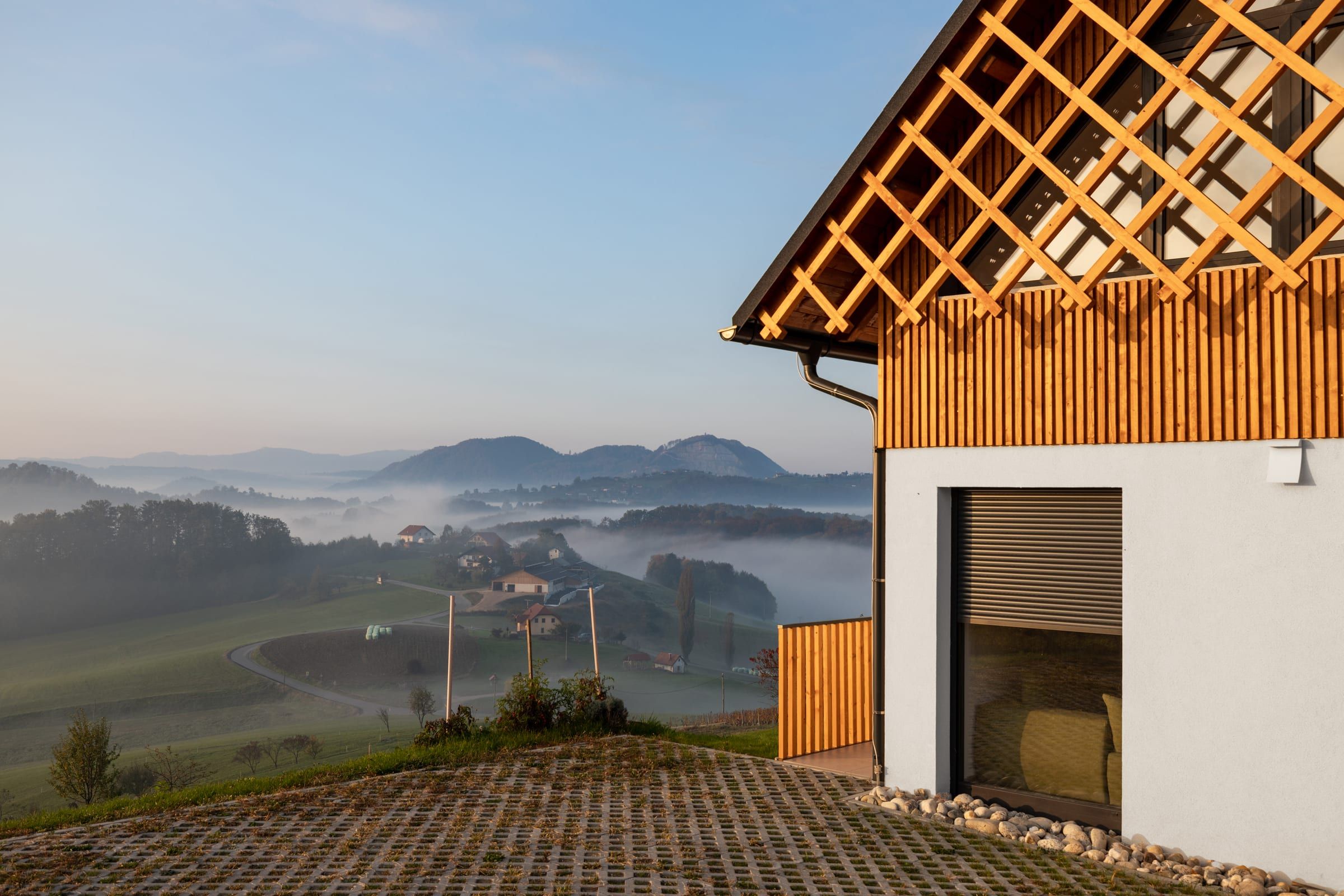 The villa's timber-slatted terrace and gable seen against the misty valley at dawn.